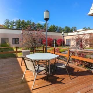 A serene outdoor patio area with a table and chairs, surrounded by blooming trees under a clear blue sky.