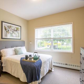 A cozy bedroom with soft lighting, featuring a neatly made bed and a large window overlooking the garden.