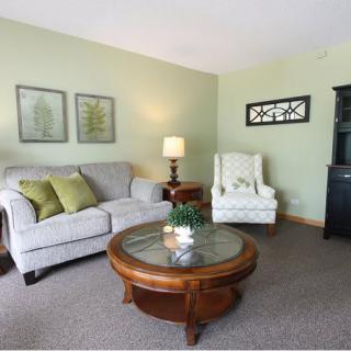 A cozy living room with a sofa, armchair, and wooden coffee table, accented by green walls and decorative artwork.