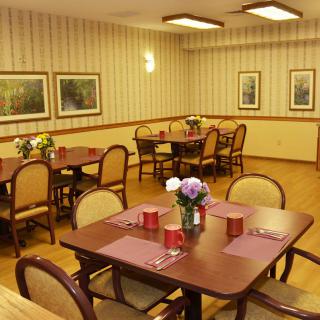 A cozy dining area with neatly arranged tables and chairs, featuring floral centerpieces and wall art.
