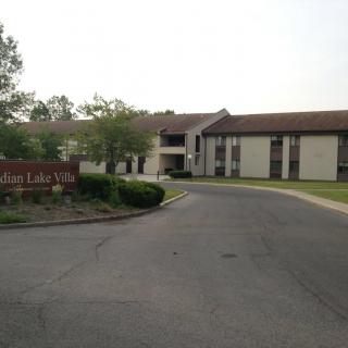 A two-story building with a driveway, surrounded by trees and grass.