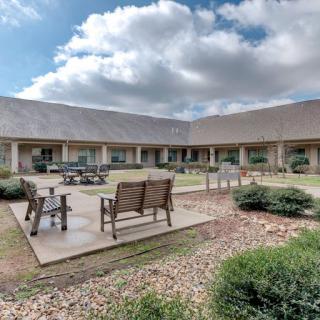 A serene courtyard with outdoor seating and lush landscaping under a partly cloudy sky.