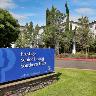 A senior living facility with a landscaped exterior and prominent signage under a clear blue sky.