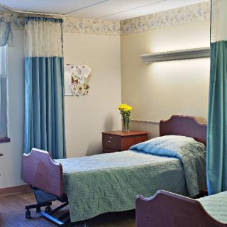 A hospital room with a bed, curtains, and a vase of flowers on the nightstand.