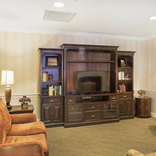 A cozy living room with a large entertainment center featuring a television and shelves, surrounded by comfortable armchairs and warm lighting.