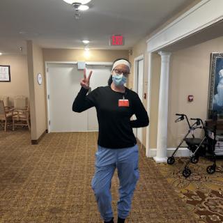 A cheerful individual wearing a mask and casual clothing poses playfully in a hallway.
