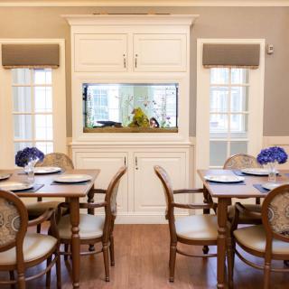 A stylish dining room featuring an aquarium built into the wall, with elegantly set tables and chairs adorned with purple flowers.