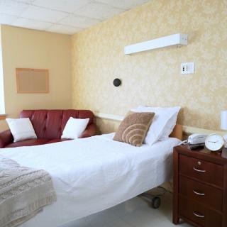 A hospital room with a neatly made bed and a couch in the corner.