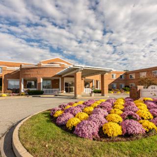 A welcoming healthcare facility surrounded by vibrant flowers and a picturesque cloudy sky.