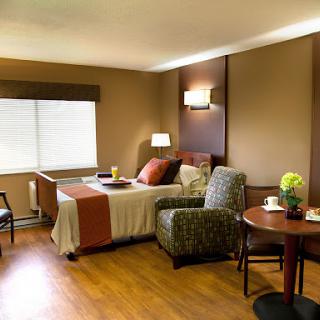 A cozy and well-furnished hotel room featuring a bed, armchair, and a small dining table.