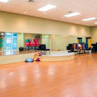 An empty dance studio featuring a hardwood floor, large mirrors, and various exercise equipment.