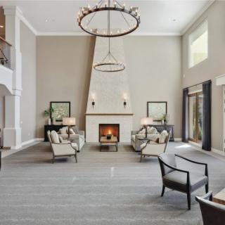A spacious living room with modern decor, featuring a fireplace and high ceilings adorned with elegant chandeliers.