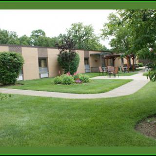 A view of a building surrounded by a well-maintained garden with a pathway and lush green lawn.