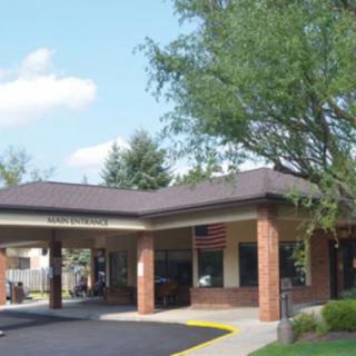 A building entrance with a covered driveway, surrounded by trees under a clear sky.