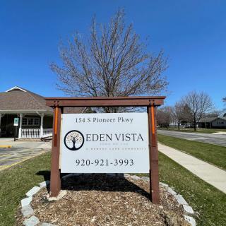 A wooden sign for Eden Vista located on a landscaped area, with a clear blue sky and building in the background.
