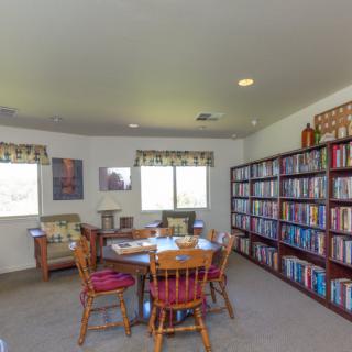 A cozy library room with bookshelves, a table with chairs, and windows letting in natural light.