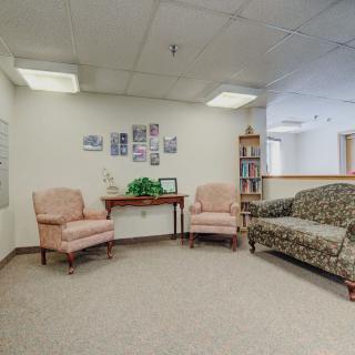 A cozy waiting room with chairs and a sofa arranged around a small table, featuring simple decor on the walls.