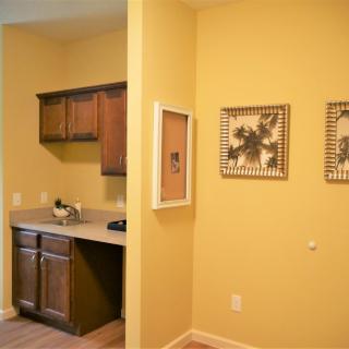 A cozy kitchen area with yellow walls and wooden cabinets, adorned with framed artwork.