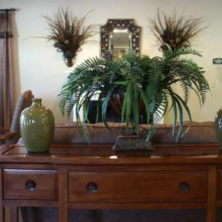 A wooden console table adorned with green vases and plants, positioned below a decorative mirror.