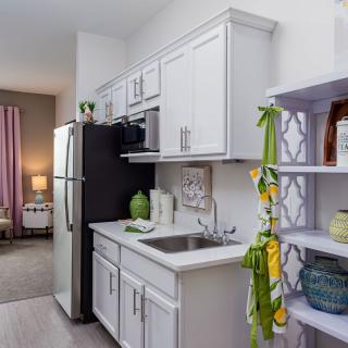 A modern apartment kitchen with white cabinets and a black refrigerator.