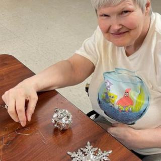 A woman sitting at a table and working on crafting decorations, smiling warmly.