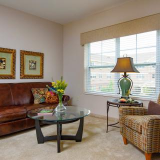 A cozy living room with a leather sofa, glass coffee table, and a floor lamp by the window.