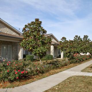 A building with a landscaped walkway lined with trees and shrubs on a clear day.