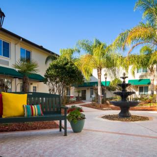 A serene courtyard featuring a central fountain surrounded by palm trees and a seating area.