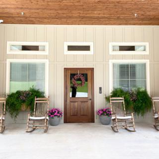 A welcoming porch with wooden rocking chairs, plants, and a wooden door.