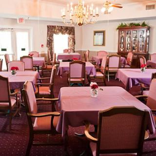 A well-arranged dining room with tables and chairs covered in pink tablecloths, illuminated by a chandelier.