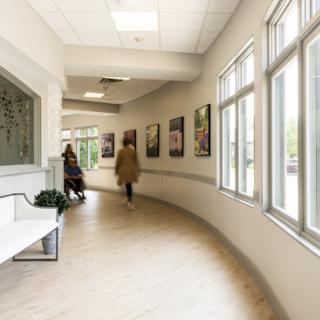 A modern and well-lit hallway in a healthcare facility, featuring large windows and artwork on the walls.