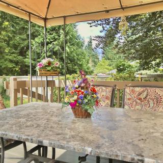 A tranquil patio setup featuring a marble table adorned with a vibrant flower arrangement, surrounded by lush greenery under a canopy.