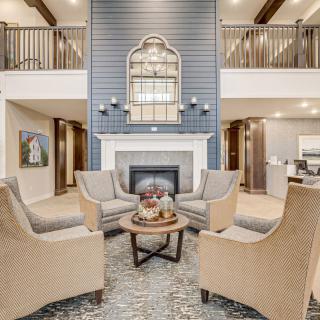 A modern living room with a central fireplace, surrounded by four upholstered chairs and decorated with a large mirror above the mantle.