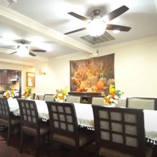A spacious dining room featuring a long table set with decorative items and surrounded by chairs, under the glow of ceiling fans and wall art.