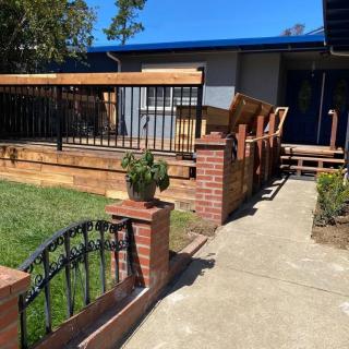 A house with a wooden deck, surrounded by a garden and brick fence.