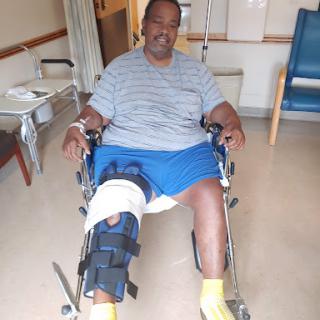 A patient sitting in a wheelchair with a knee brace, recovering in a hospital setting.