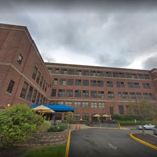 A large brick building with multiple windows and a covered entrance under a cloudy sky.