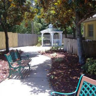 A peaceful garden pathway with benches leading to a gazebo surrounded by trees and a fence.