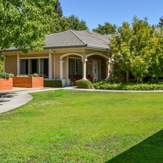 A charming single-story house surrounded by a well-maintained yard with lush greenery and trees.