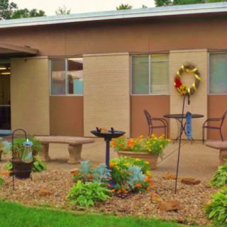 A charming garden patio with outdoor seating, decorative wreath, birdbath, and lush plants.