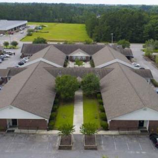 Aerial view of a complex with multiple buildings and a parking lot, surrounded by greenery.