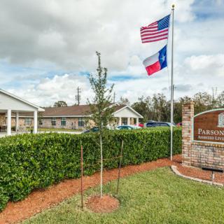 A landscaped area with American and Texas flags displayed near a building and a sign.