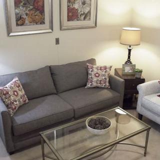 A cozy living room featuring a gray sofa, patterned pillows, and a glass coffee table.