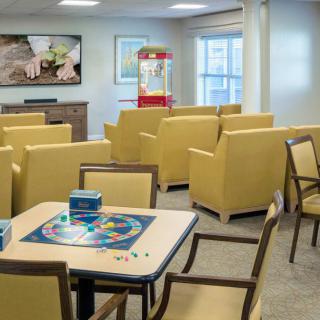 A cozy living room with yellow chairs, a game table, a large television, and a popcorn machine.
