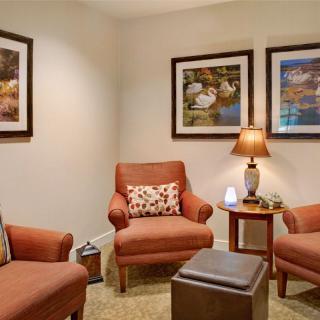A cozy seating area with comfortable armchairs, a side table with a lamp, and framed art on the walls.