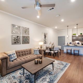 A modern open-concept living room and kitchen with stylish decor, featuring a comfortable sofa, coffee table, dining area, and contemporary lighting.