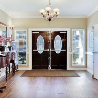 A well-lit foyer with double doors, windows, and a chandelier overhead.