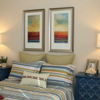 A cozy bedroom with striped bedding, framed wall art, and elegant lighting.