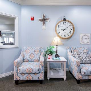 A cozy seating area with patterned chairs, a side table, and a large wall clock.