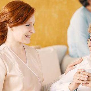 A nurse smiling and interacting with an elderly person, offering support and care.